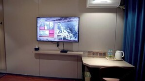 Ein Hotelzimmer mit flachbildfernseher an der Wand, einem kleinen Schreibtisch mit Stuhl, einer Kaffeemaschine und einem Mülleimer.