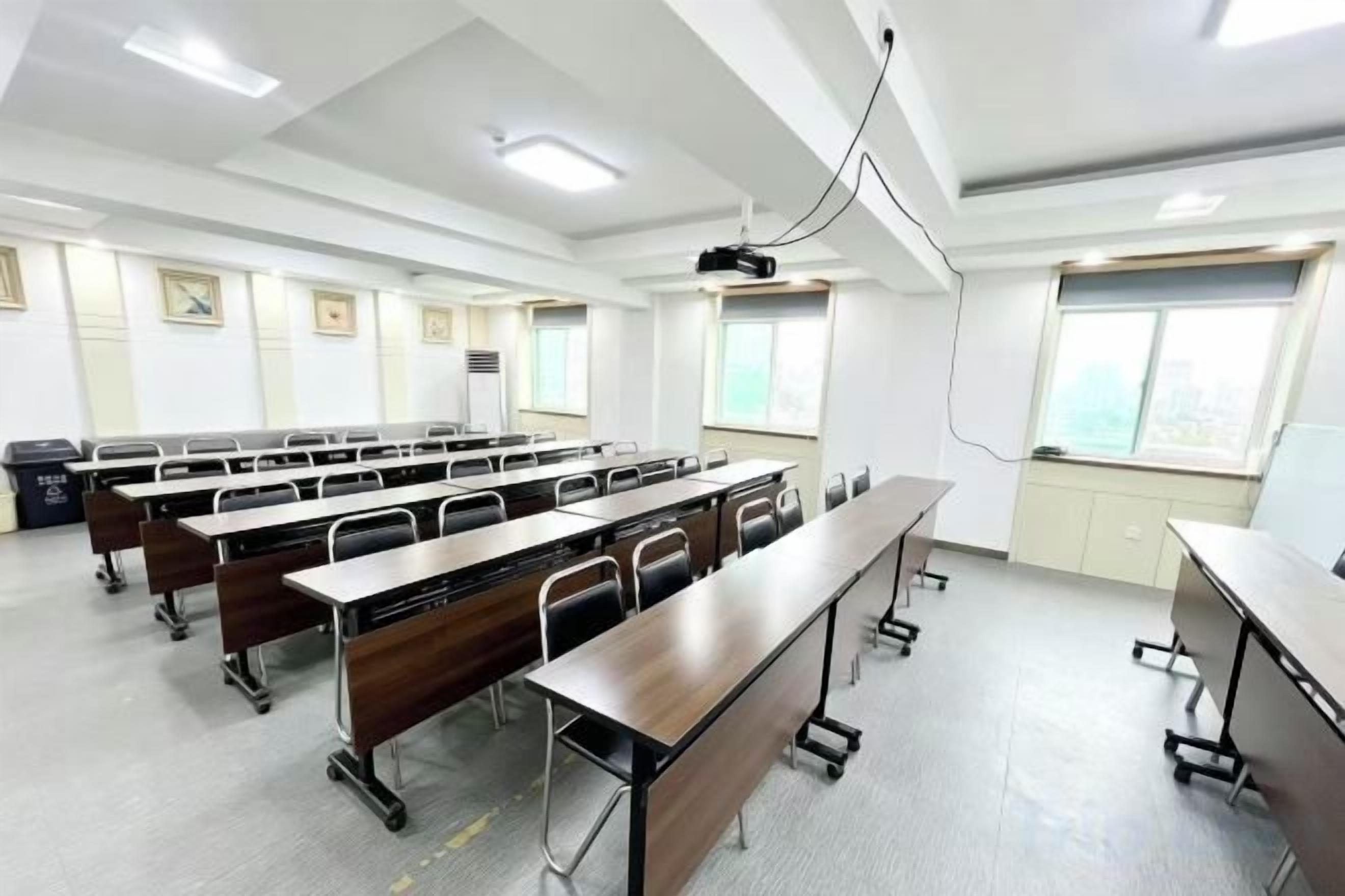 Ein Klassenzimmer mit Reihen von Tischen, einem Projektor und einem Fenster mit Jalousien.
