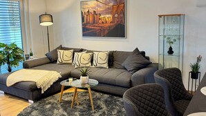A modern living room with a grey sofa, a round coffee table, and a large cityscape painting on the wall.