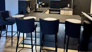 A modern kitchen with a central island, bar stools, and a dining area.