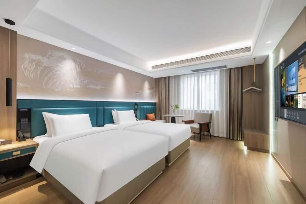 Habitación de hotel con dos camas, un escritorio, una silla, un televisor y una ventana con cortinas.