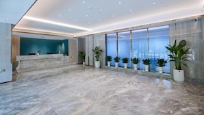 A spacious lobby with a marble floor, a reception desk, and a row of potted plants. - Elong Anyun Hotel (Nantong Haohe Scenic Area Zhongxiu West Road Subway Station) (Nantong)