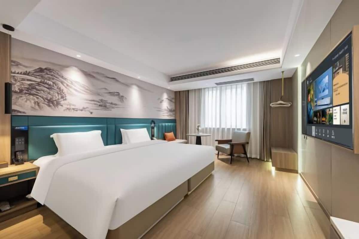 Habitación de hotel con cama, escritorio, silla, televisor y pared con mural.