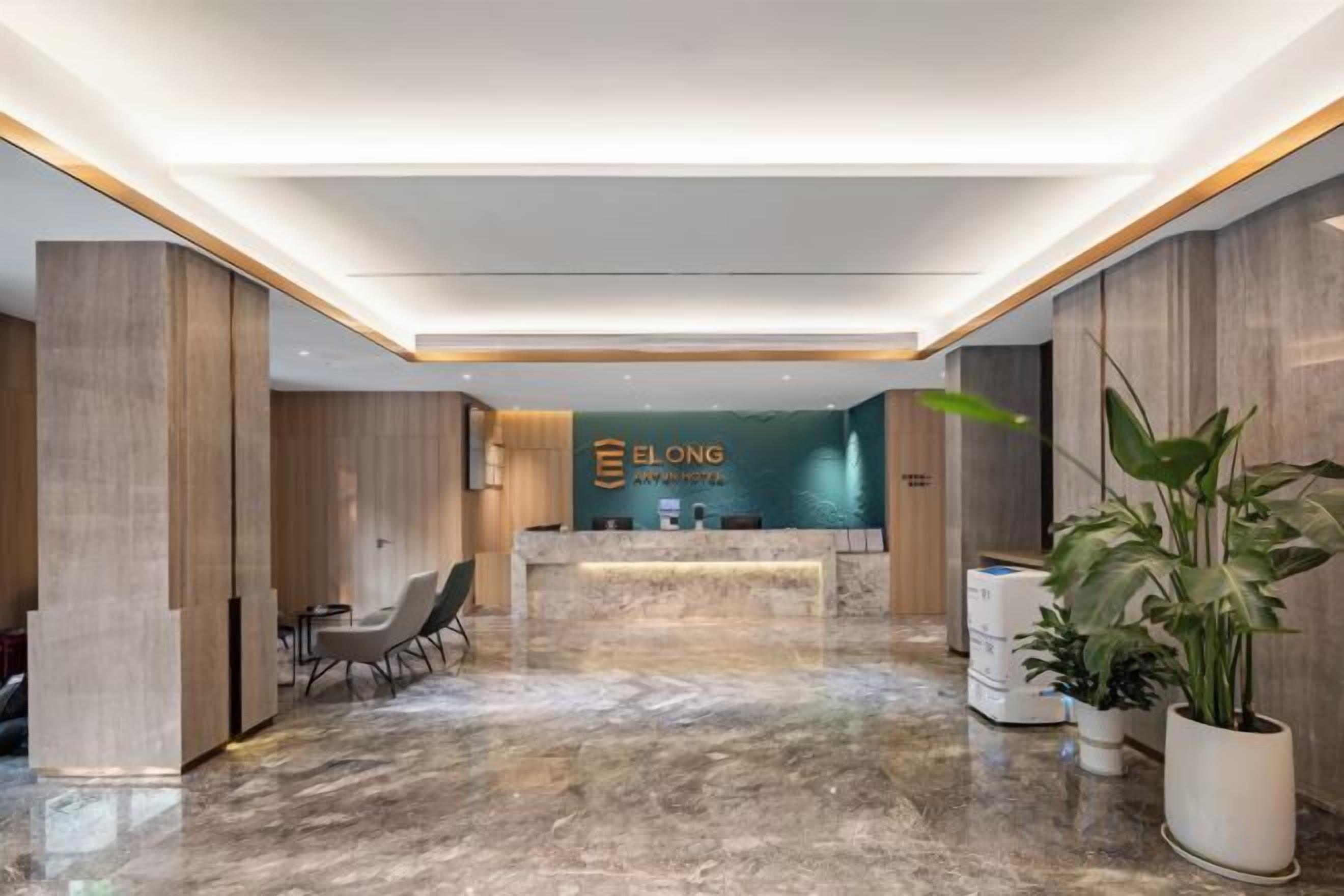 A hotel reception area with a marble floor, reception desk, seating area, and potted plants.