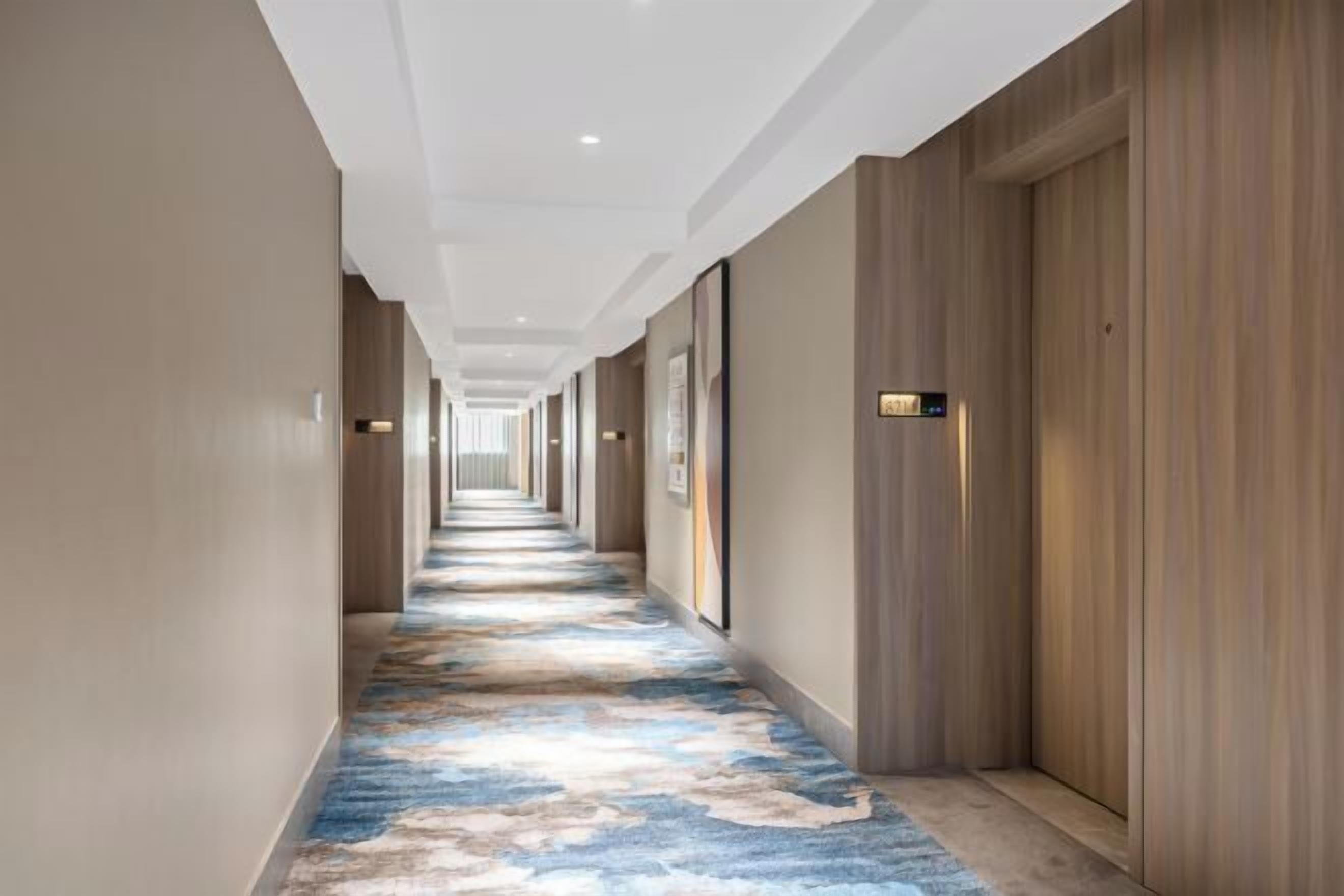 Un pasillo de hotel con alfombra estampada, paneles de madera y varias puertas a lo largo del corredor.