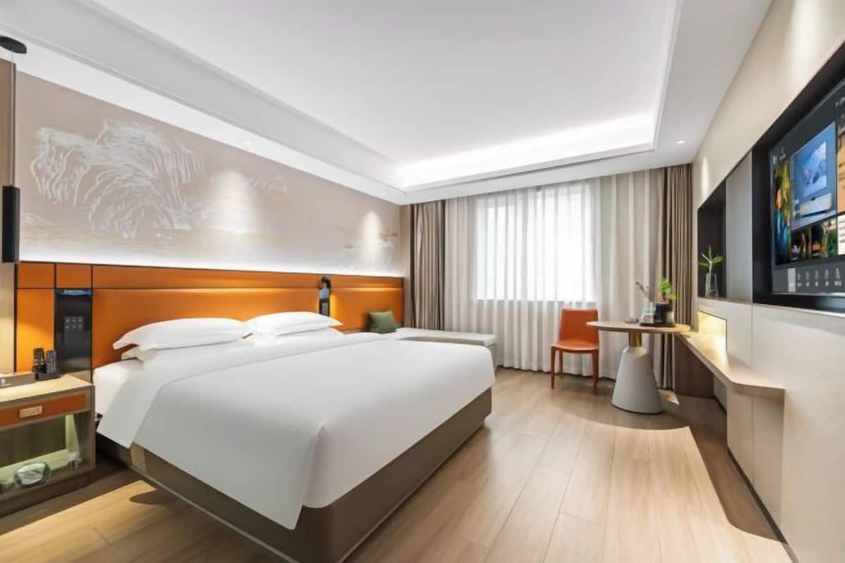 Una habitación de hotel moderna con una cama grande, un escritorio, un televisor y una obra de arte colgada en la pared.