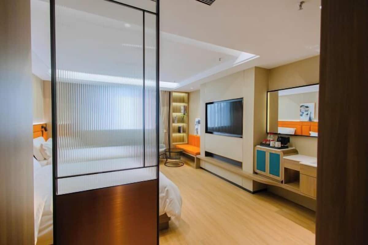 Una habitación de hotel moderna con una cama grande, televisión, sofá y un pequeño rincón de descanso.