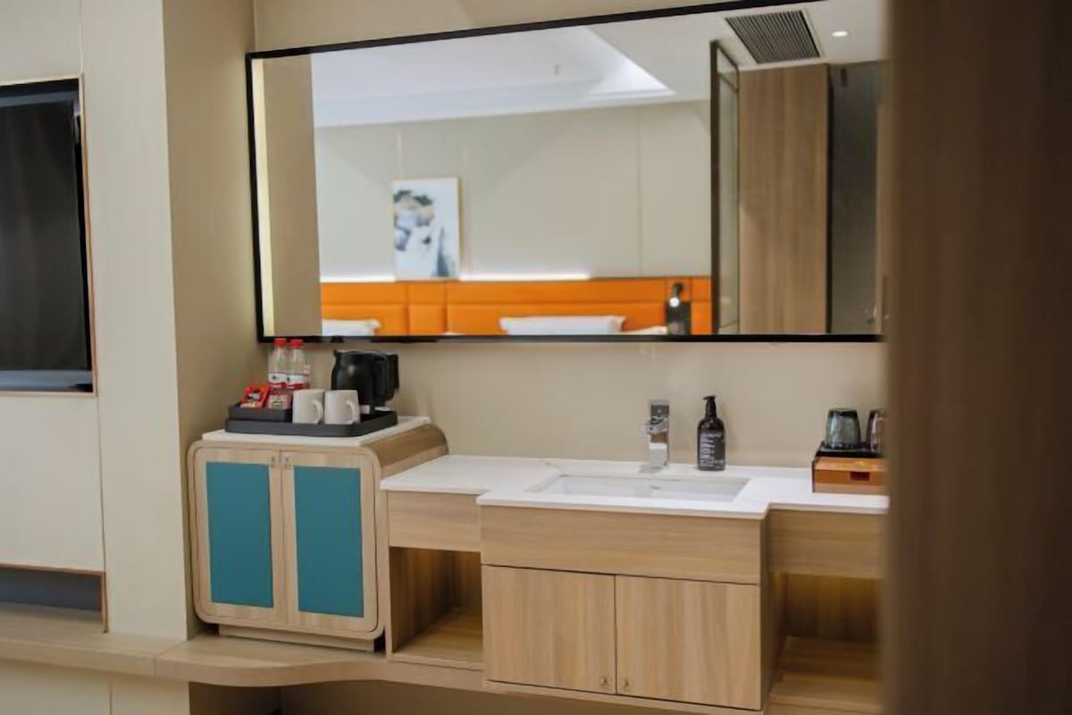 A modern bathroom with a large mirror, a sink, and a cabinet with teal doors.