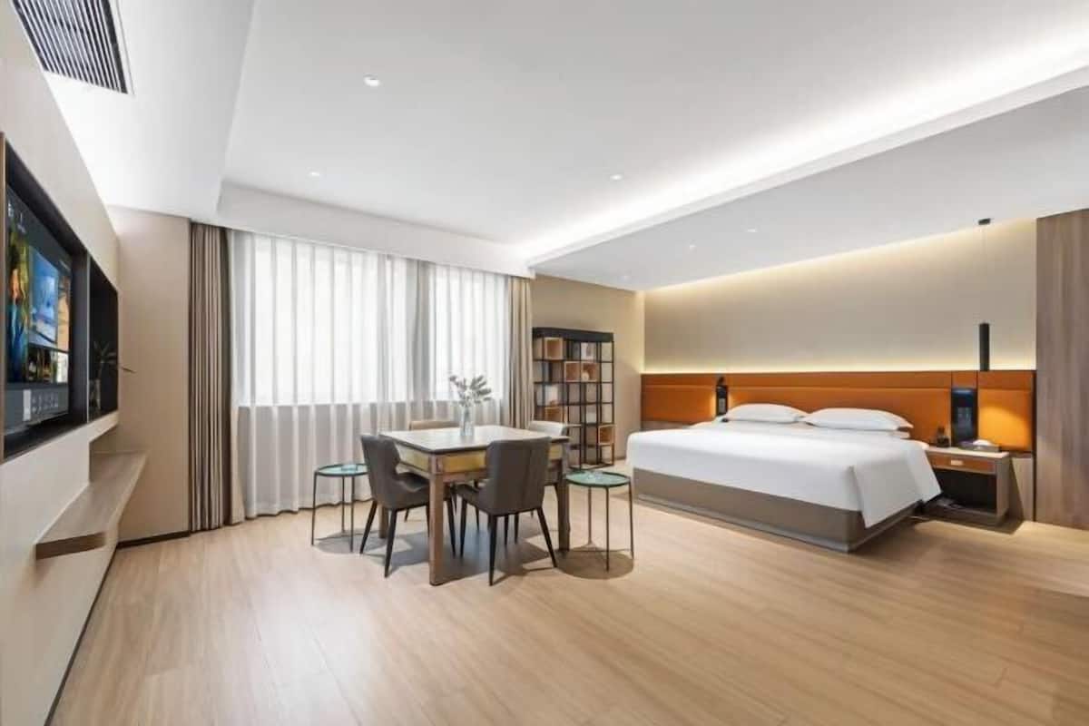 Una habitación de hotel moderna con una cama, mesita de noche, lámpara, televisor y un rincón de comedor con sillas y mesa.