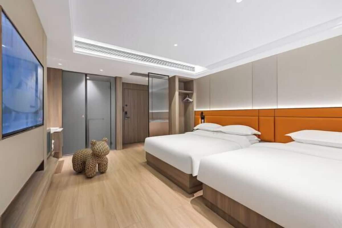 Habitación de hotel con dos camas, un televisor de pantalla plana grande, un adorno de oso de peluche y un armario.