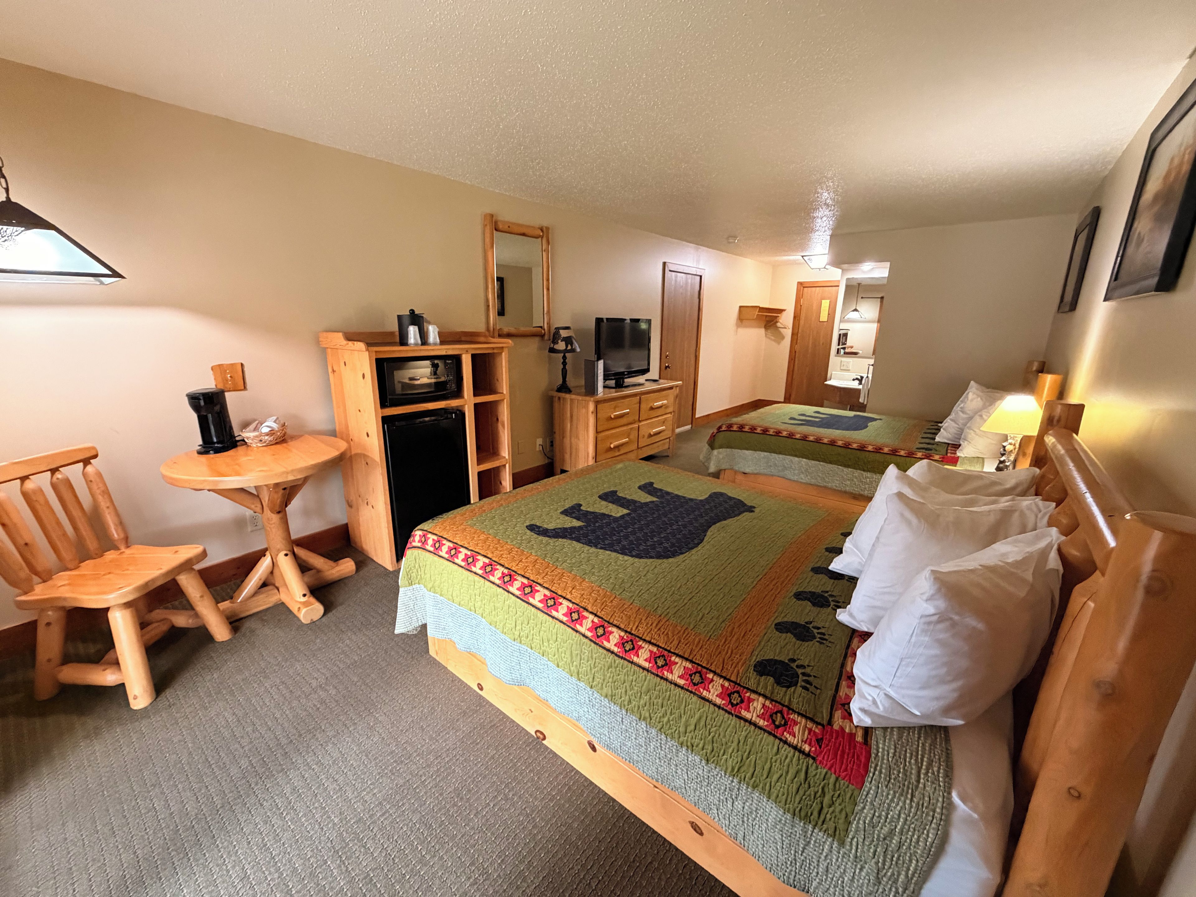 Quarto de hotel com duas camas, uma escrivaninha de madeira, televisão e um espelho.