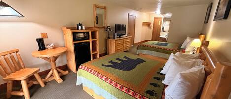 A hotel room with two beds, a small wooden desk, a television, and a mirror.