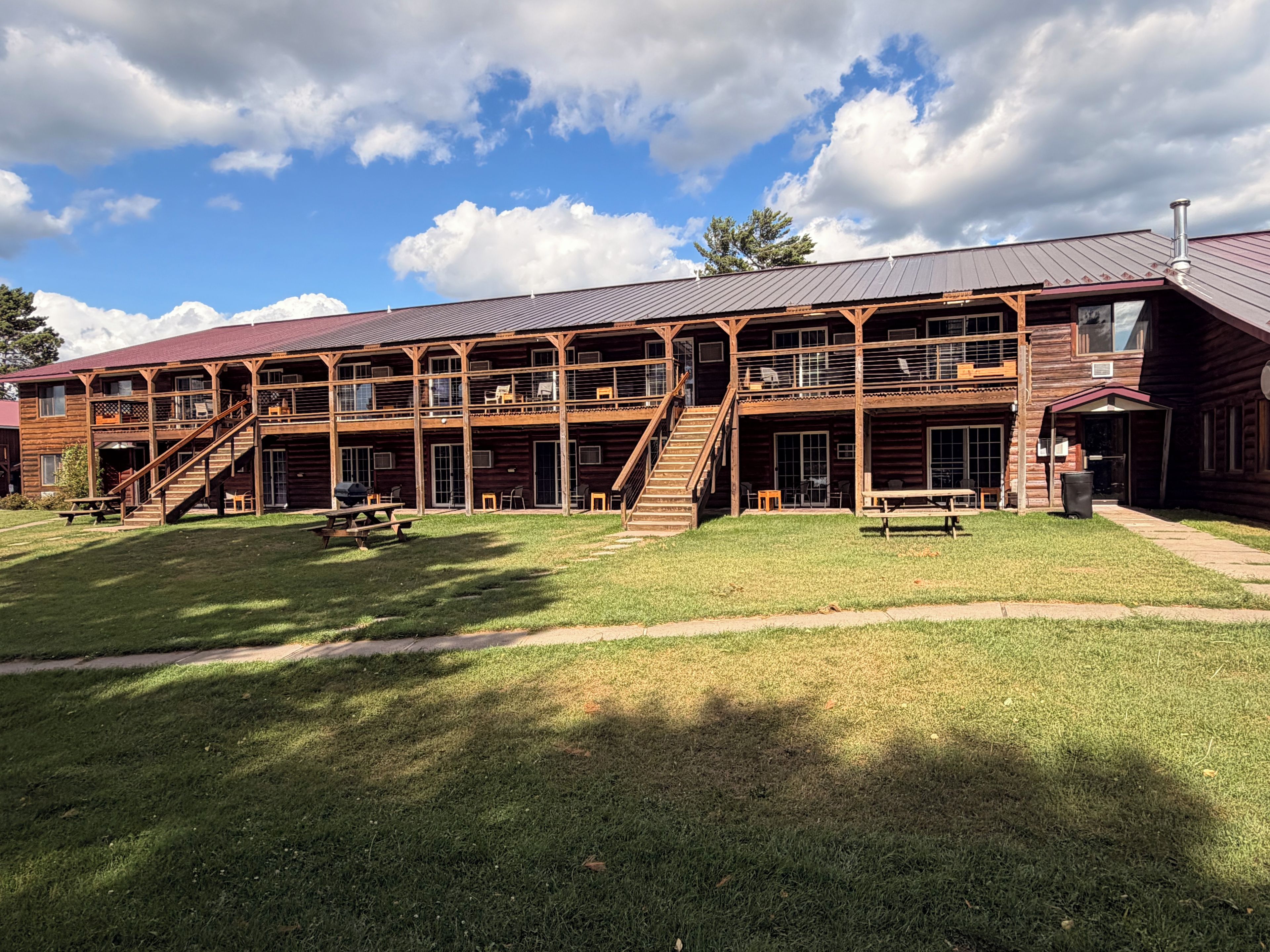 A two-story wooden building with a covered outdoor seating area and a staircase leading to the upper level.