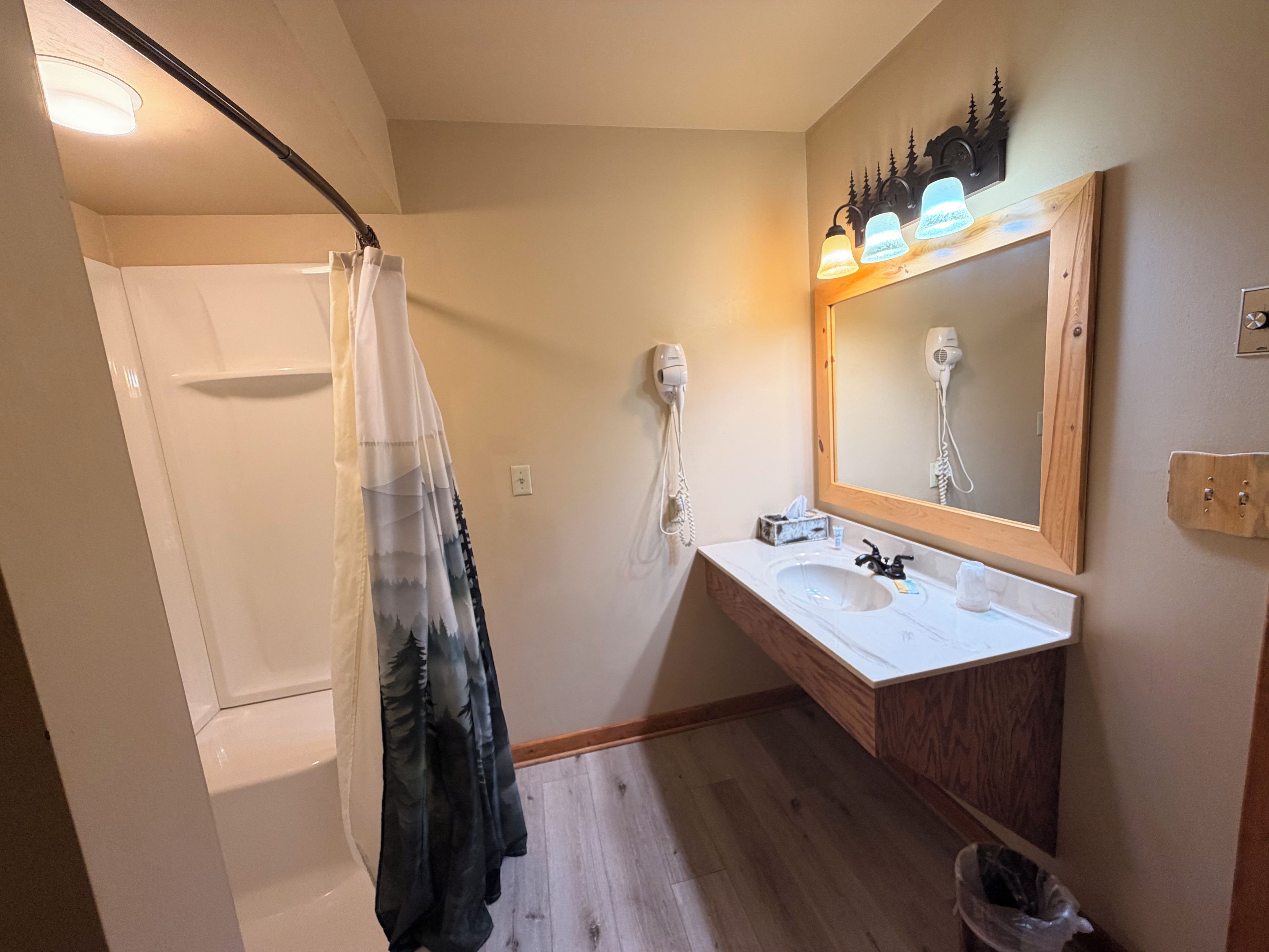 Un baño con ducha, tocador con espejo y secador de pelo en la pared.