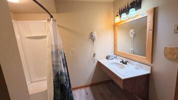 Un baño con ducha, tocador con espejo y secador de pelo en la pared.