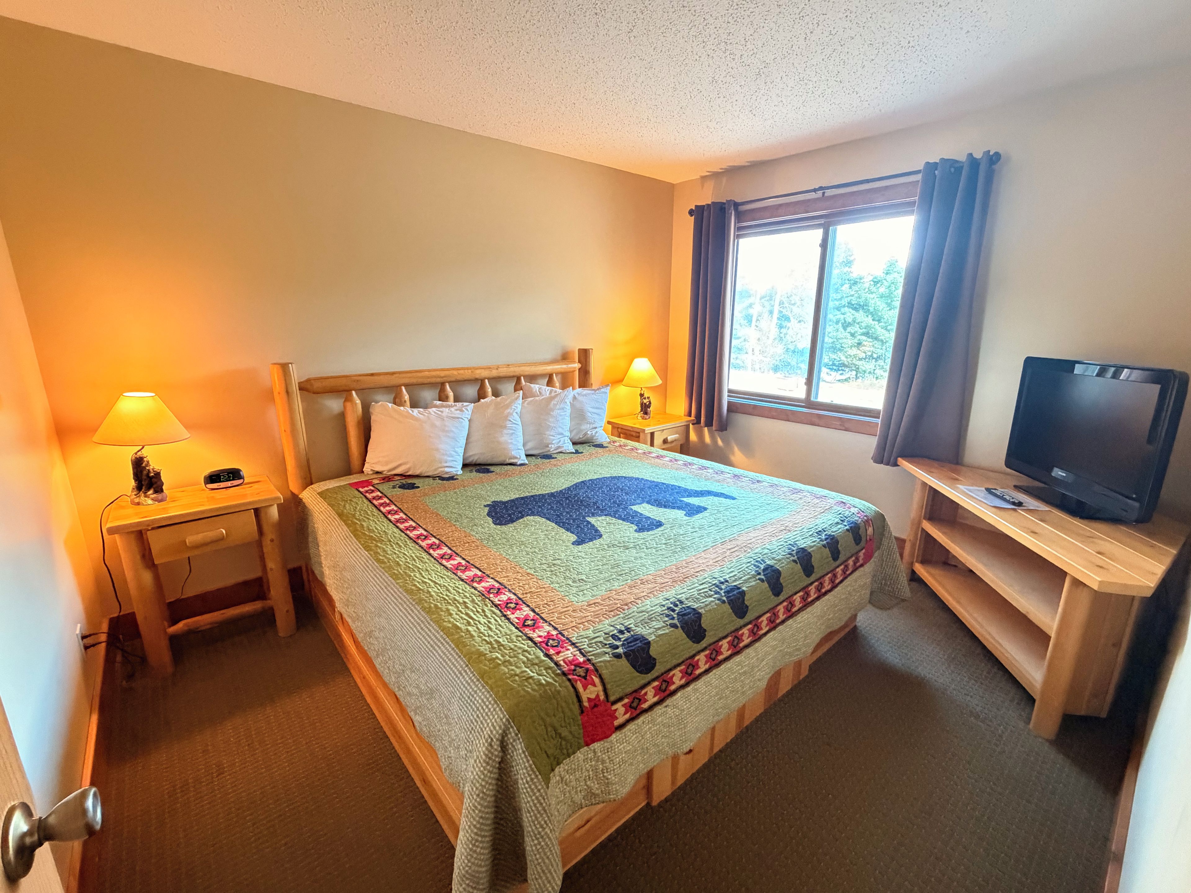 A hotel room with a bed, two bedside tables, a TV on a stand, and a window with curtains.