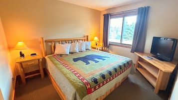 Une chambre d’hôtel avec un lit, deux tables de chevet, un téléviseur posé sur un meuble et une fenêtre avec des rideaux.