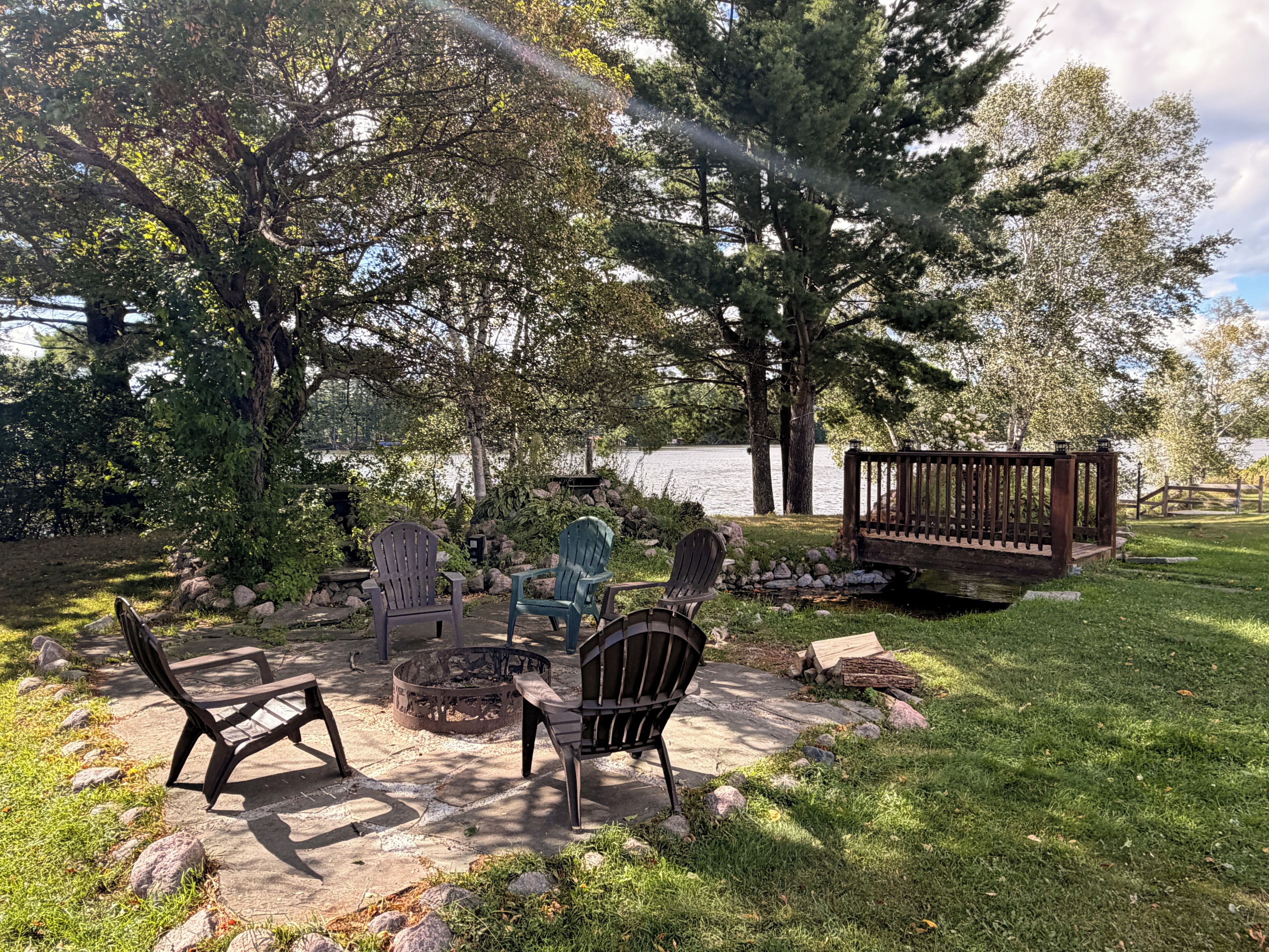 Un patio con sillas Adirondack, un hogar para fuego y una terraza de madera con vista al lago.