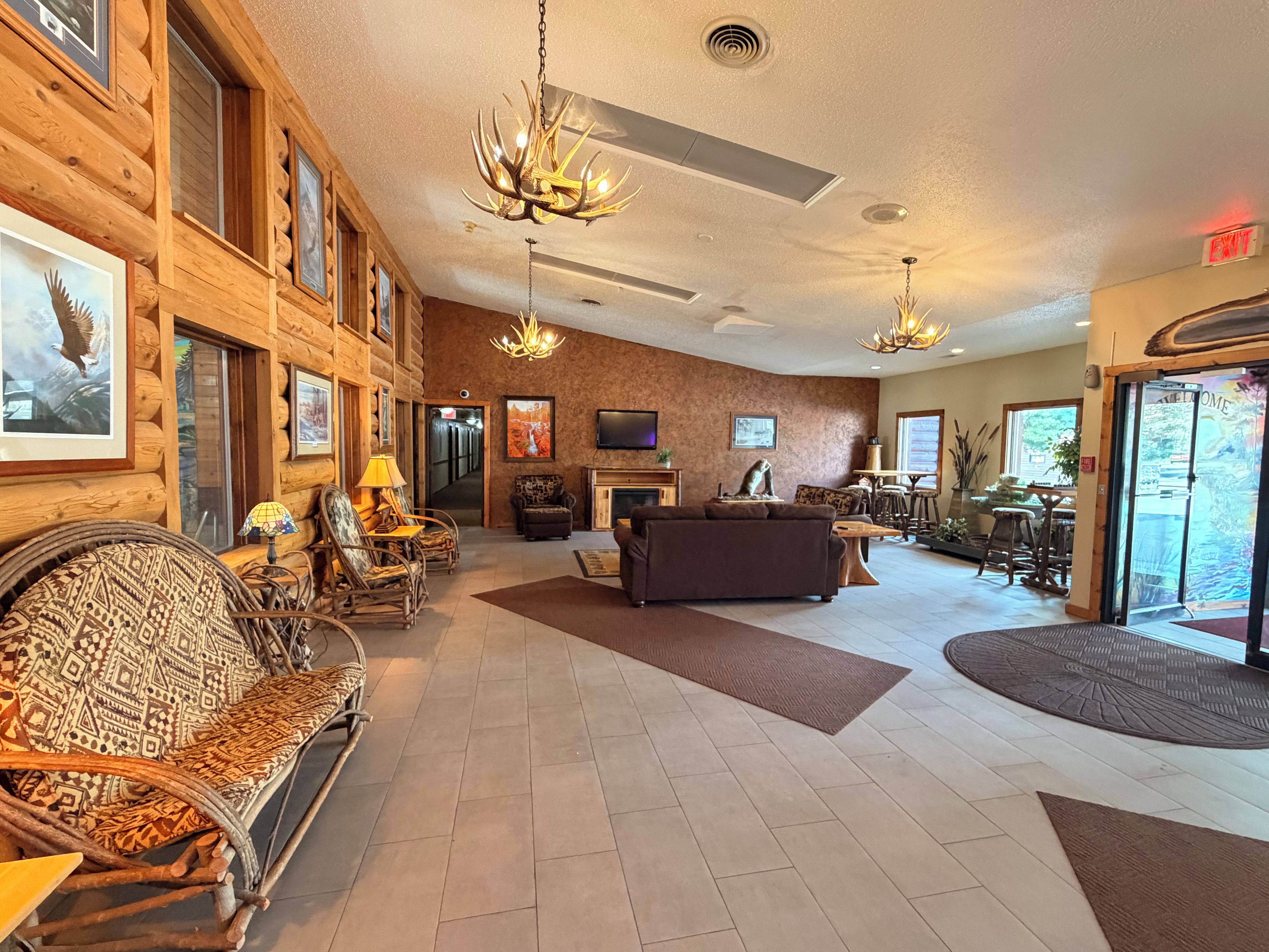 A log cabin-style interior with a fireplace, a sofa, a dining area, and a large window.