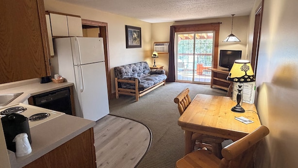 A compact kitchen with a refrigerator, stove, and wooden cabinets. A dining area with a table and chairs is adjacent to a sofa. - Eagle River Inn and Resort  (Eagle River)