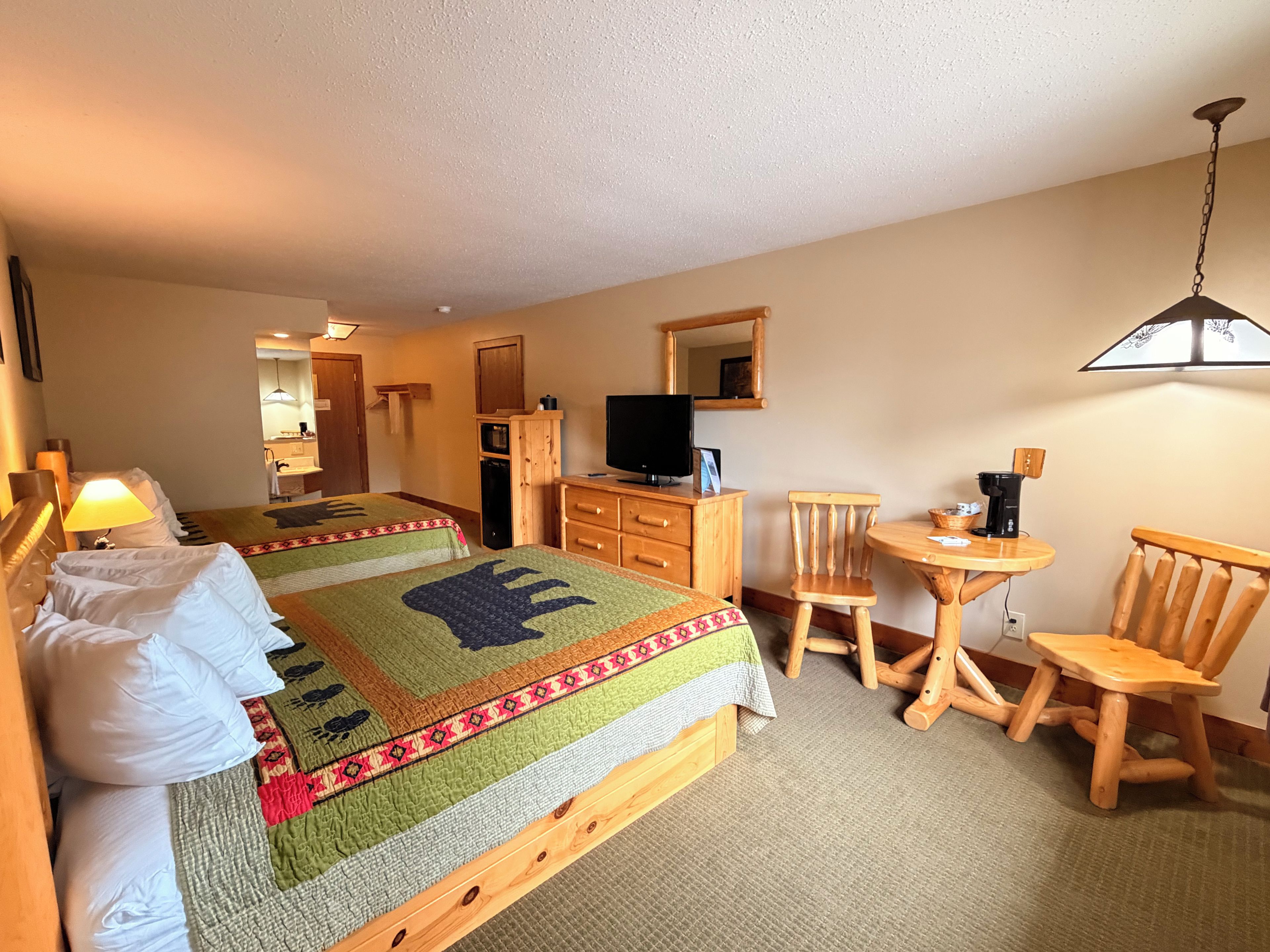 A hotel room with two beds, a television, a desk with a chair, and a small table with a chair.
