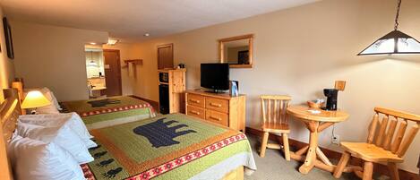A hotel room with two beds, a television, a desk with a chair, and a small table with a chair.