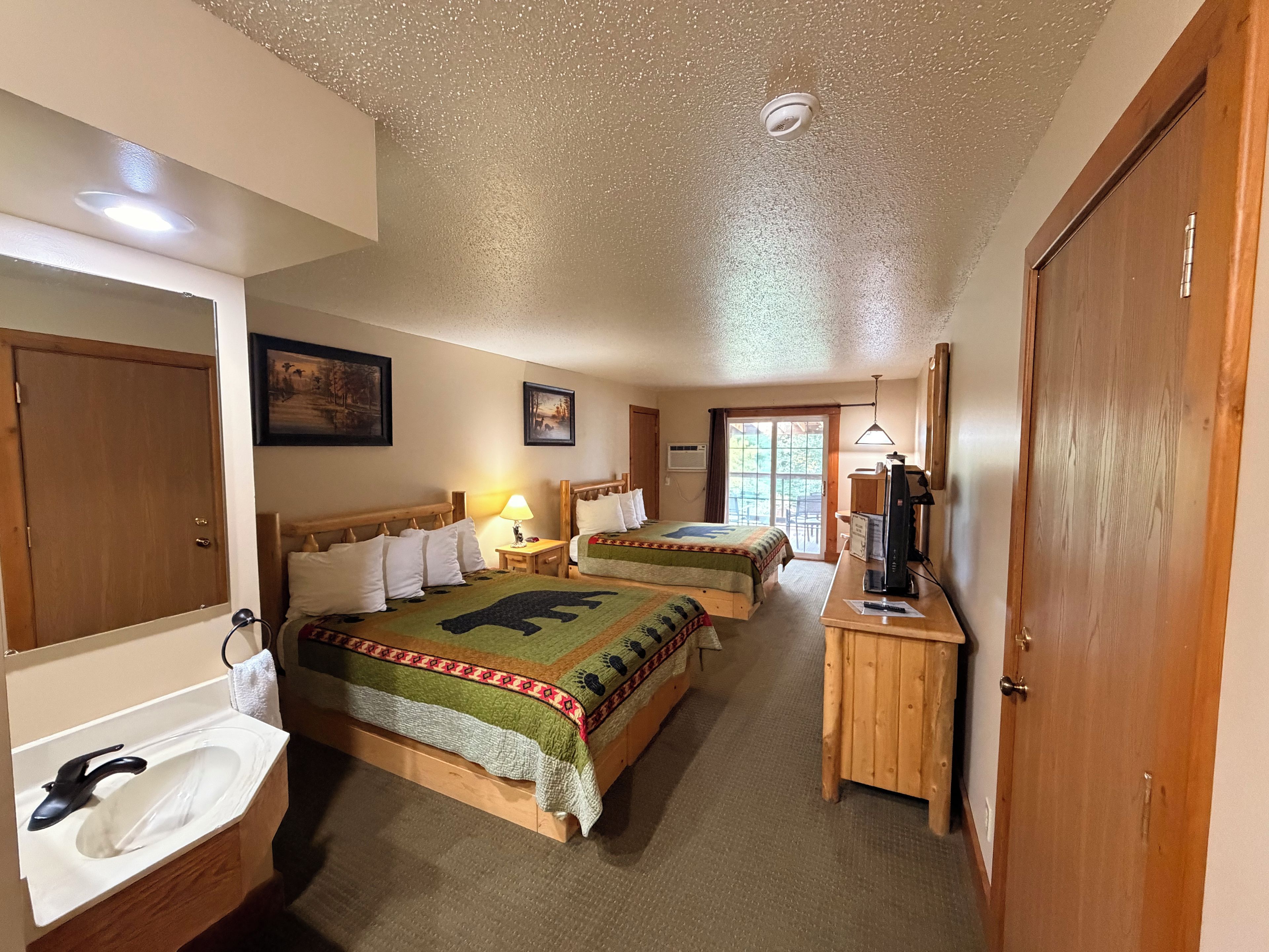 A hotel room with two beds, a bathroom, a desk with a computer, and a door.