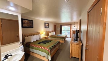 A hotel room with two beds, a bathroom, a desk with a computer, and a door.