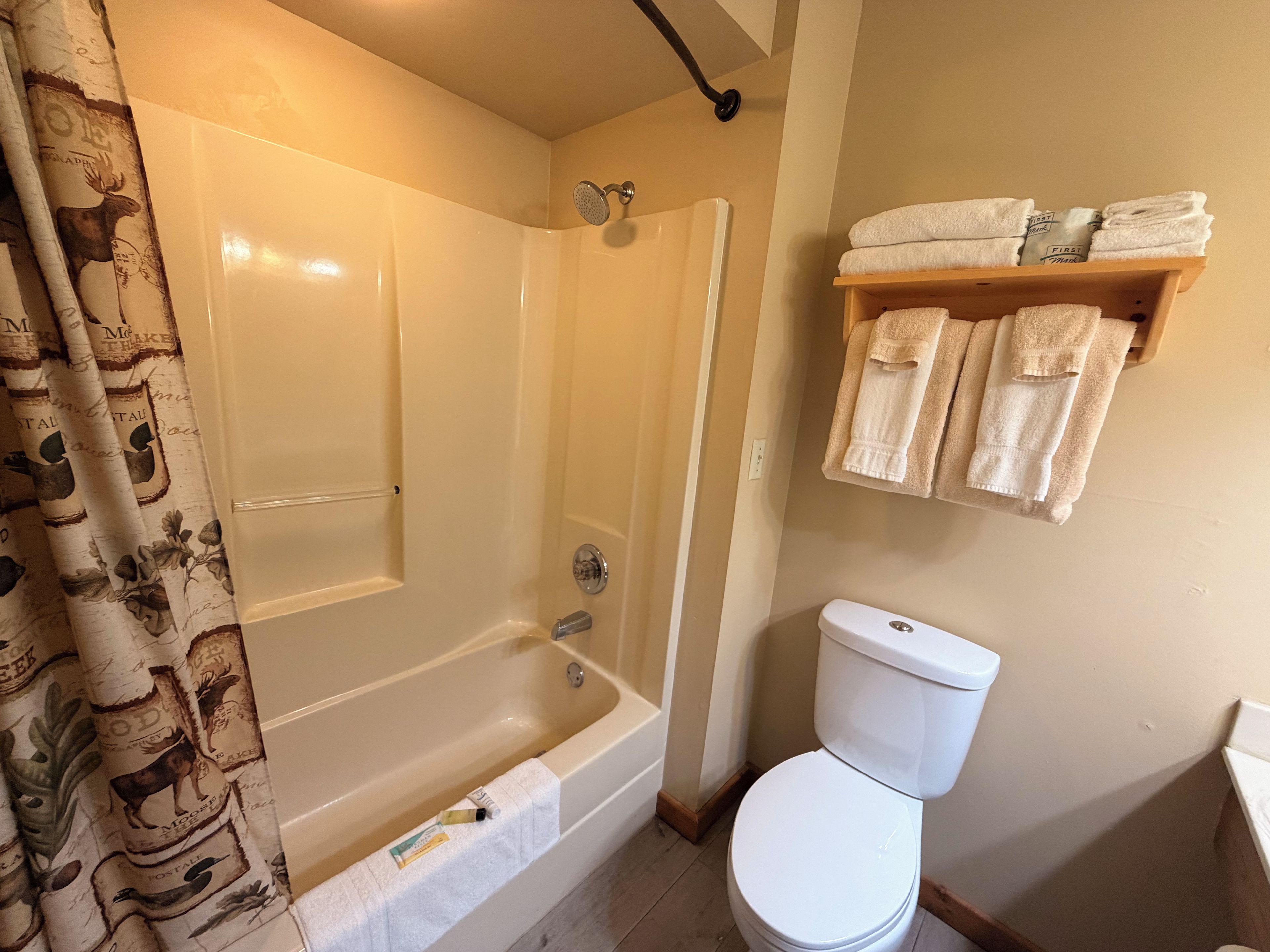 A bathroom with a bathtub, toilet, and a shelf with towels.