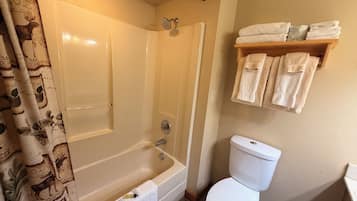 A bathroom with a bathtub, toilet, and a shelf with towels.