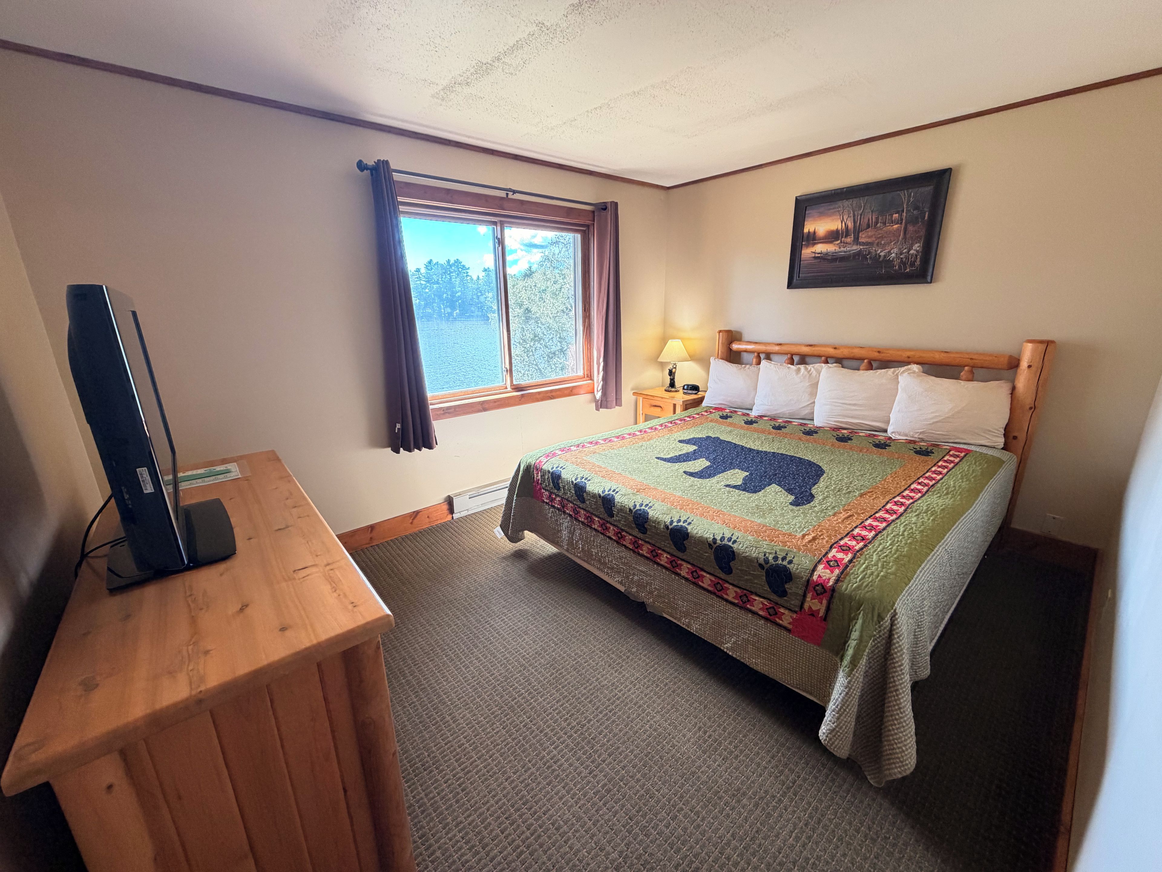 A hotel room with a bed, a desk, a television, a window with curtains, and a painting on the wall.