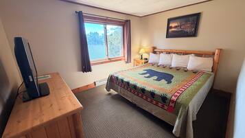 A hotel room with a bed, a desk, a television, a window with curtains, and a painting on the wall.