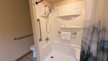 A bathroom with a glass-enclosed shower, a toilet, and a shelf with toiletries.