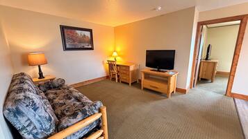 Ett vardagsrum med en soffa, ett skrivbord med en stol, en tv och en lampa.