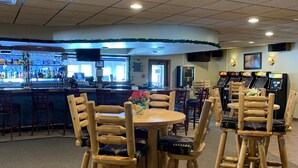 Un restaurant avec des tables et des chaises en bois, un coin bar avec des bouteilles et un écran de télévision.
