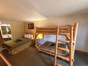 A room with two bunk beds, a wooden desk with a mirror, a small bedside table with a lamp, and a framed picture on the wall. - Eagle River Inn and Resort  (Eagle River)