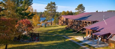 Una cabaña con techo rojo, terraza de madera y vista a un lago.