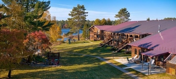 Una cabaña con techo rojo, terraza de madera y vista a un lago.