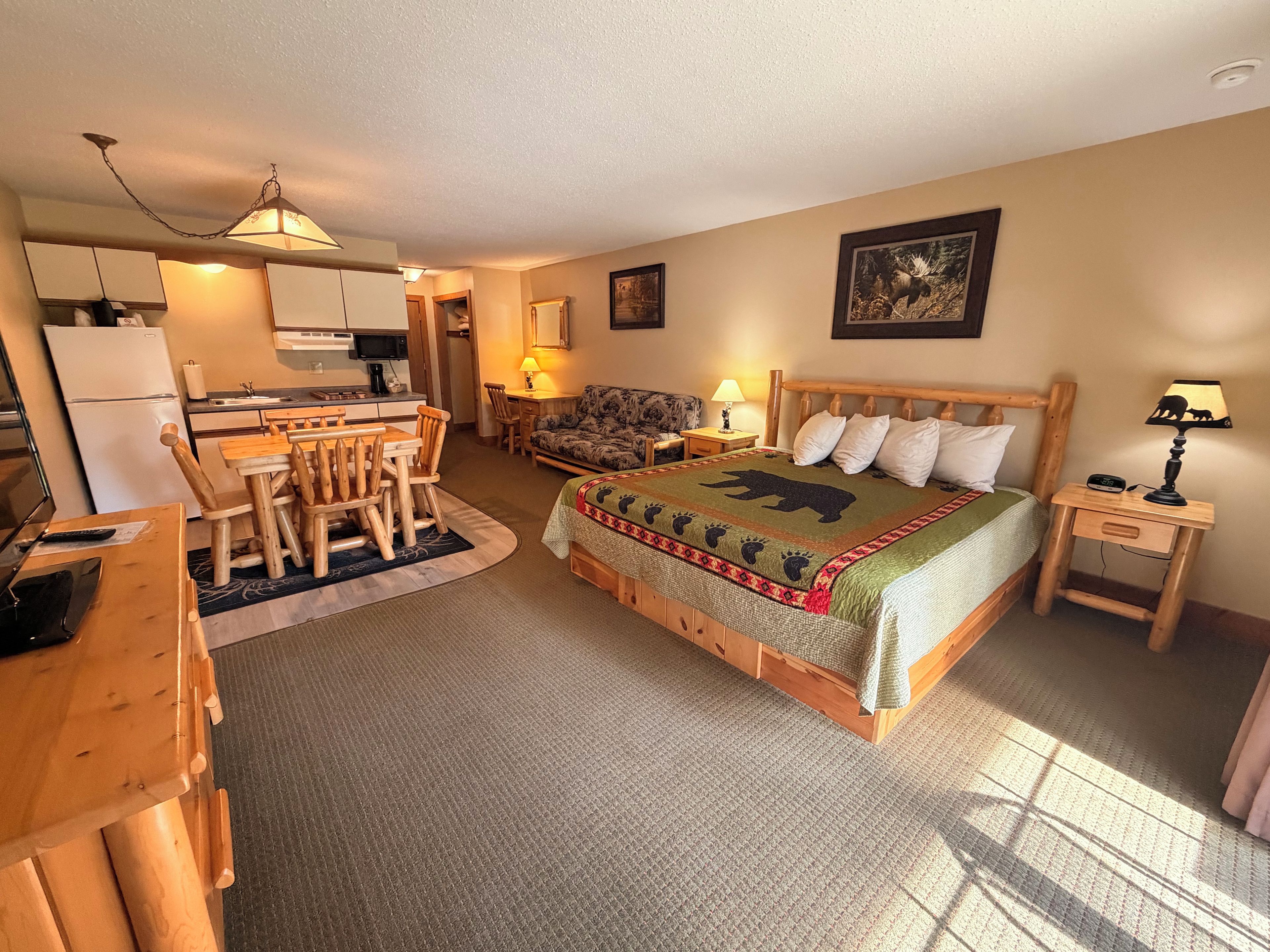 A cozy room with a bed, a dining table, chairs, a small kitchen area, and a television.