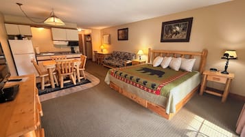 A cozy room with a bed, a dining table, chairs, a small kitchen area, and a television.