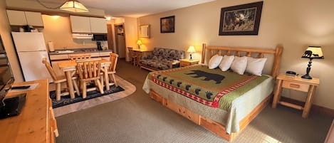 A cozy room with a bed, a dining table, chairs, a small kitchen area, and a television.
