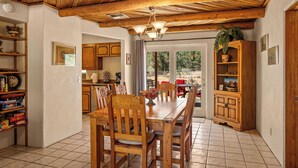 Un coin repas avec une table et des chaises en bois, un lustre et une cuisine en arrière-plan.