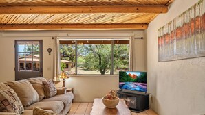 Un salon chaleureux avec un plafond en bois, une grande fenêtre donnant sur les arbres, un téléviseur et une table basse en bois.