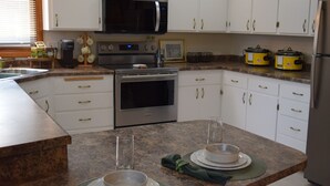A modern kitchen with white cabinets, a built-in microwave, oven, and a large island with stools. - The Birchwood - 1 mile from Lambeau Field! (Green Bay)