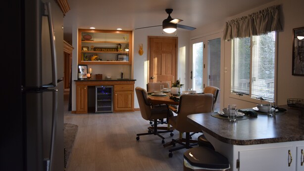 A kitchen with a dining table, chairs, a refrigerator, wooden cabinets, a built-in oven, and a ceiling fan. - The Birchwood - 1 mile from Lambeau Field! (Green Bay)