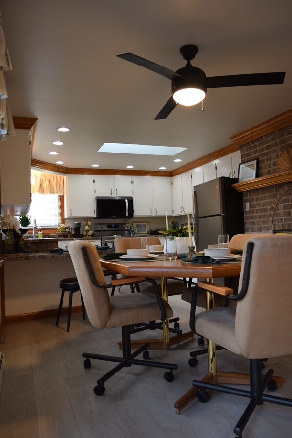 A modern kitchen with white cabinets, a black refrigerator, and a microwave. There is a dining table with four chairs.