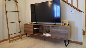 A room with a wooden TV stand, a flat-screen TV, a ladder, and a small shelf with books and a picture frame. - The Birchwood - 1 mile from Lambeau Field! (Green Bay)