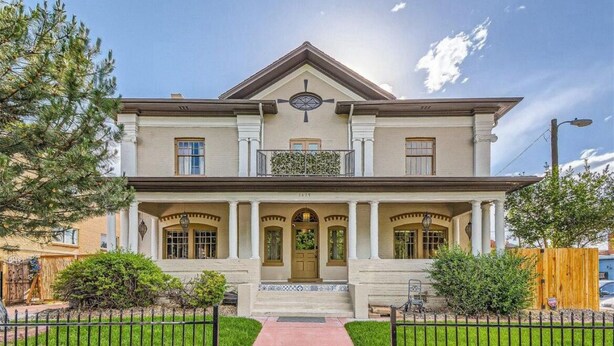 A two-story house with a symmetrical facade, a central entrance with a double door, and a small balcony above the main entrance.