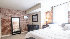 A hotel room with a brick wall, a large bed, a dresser, a mirror, and an air conditioning unit.