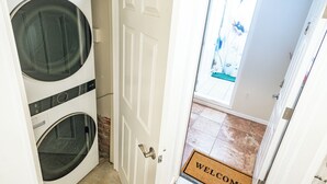 A laundry room with two front-loading washing machines and a door leading to a tiled entrance area.